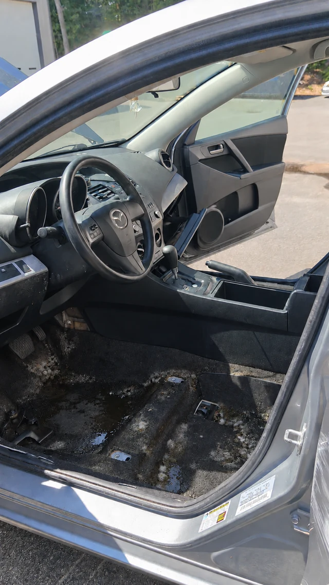 Mazda driver-seat area viewed through the open door, with water and mold shown on the carpeted floor
